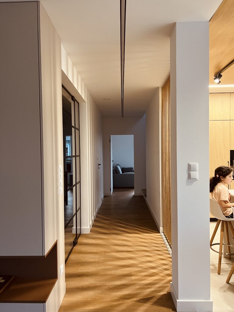 Hallway with dynamic shadows from kitchen lighting, creating a warm and lively atmosphere, designed by Musca Studio