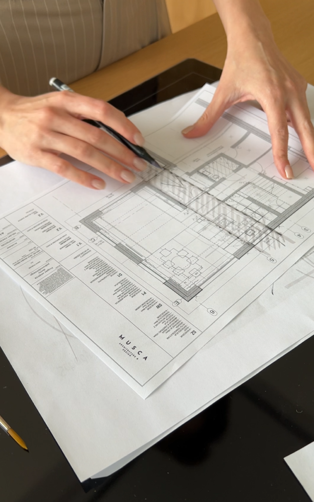 Architect reviewing detailed floor plan with pencil, Musca Studio project in progress